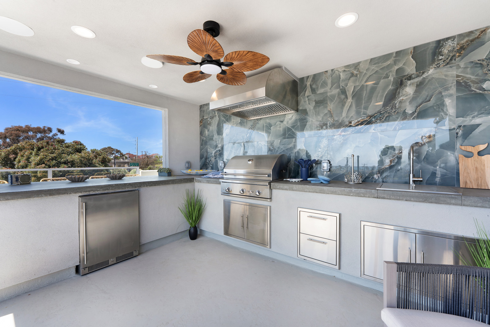 Custom outdoor kitchen featuring built-in grill, sink, refrigerator, stainless steel storage, and designer tile backsplash in San Diego.
